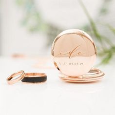 two wedding rings sitting on top of a table next to a round ring holder with the word love written on it