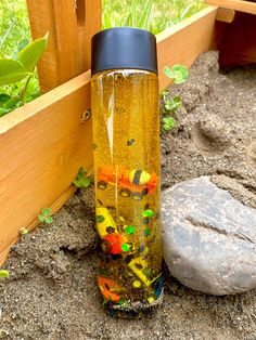 a yellow and black water bottle sitting on the ground next to a wooden fence with plants growing out of it