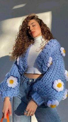 a woman with curly hair is holding an orange handbag and wearing a blue knitted cardigan