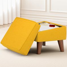 a yellow ottoman sitting on top of a white floor next to a wooden table with a magazine in it