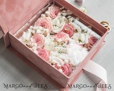 two wedding rings in a pink box with flowers on the floor next to it,