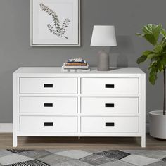 a white dresser sitting in a living room next to a lamp and potted plant