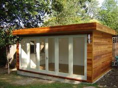 a small wooden shed with sliding glass doors on the front and side windows, in a backyard