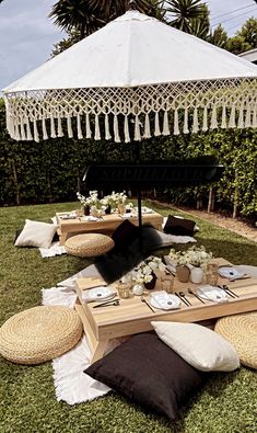 an outdoor picnic setting with white and black pillows on the grass, tablecloths and umbrella