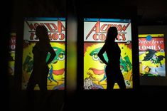 two people standing next to each other in front of comic book cover windows at night