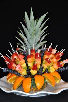 an arrangement of fruit is arranged on a white platter with pineapples, oranges and strawberries