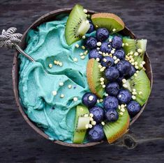 a bowl filled with blueberries, kiwis and other fruits on top of a wooden table