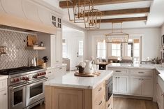 a large kitchen with white cabinets and wood beams on the ceiling, along with wooden flooring