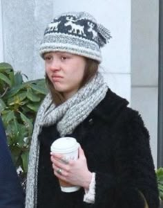 a woman holding a coffee cup and wearing a hat