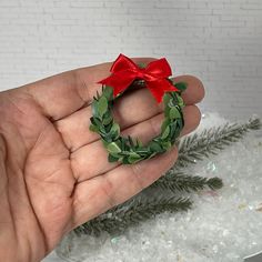 a hand holding a small wreath with a red bow