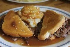 a plate topped with meat and gravy on top of a wooden table next to other plates