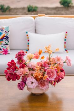 a vase filled with lots of pink and orange flowers on top of a wooden table