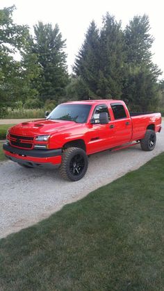 a red truck parked on the side of a road next to some grass and trees