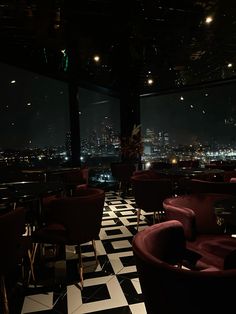 a dimly lit restaurant with black and white checkered flooring, red chairs and tables