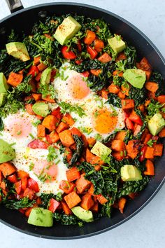 a skillet filled with eggs, vegetables and avocado on top of a table