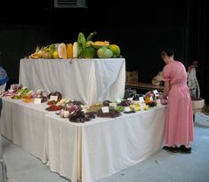 a woman standing next to a table filled with fruits and vegetables on it's sides