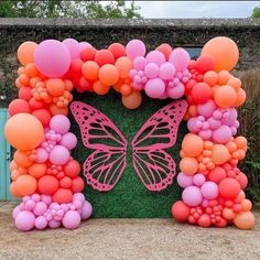 an orange and pink balloon arch with a butterfly on it