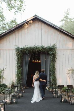 a bride and groom standing in front of a barn with greenery on the doors