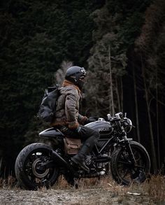 a man riding on the back of a motorcycle down a dirt road next to trees