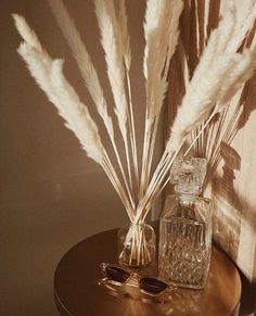 a glass vase with some white flowers and sunglasses on a small table in front of a wall