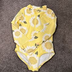 a yellow and white one piece swimsuit with sunflowers printed on it, laying on the floor