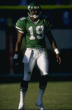 a football player standing on the field with his hands in his pockets and wearing a green uniform