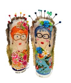 two handmade dolls are sitting next to each other with needles in their heads and flowers on them