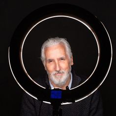 an older man with white hair and beard holding a circular object in front of his face