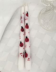 two white candles with ladybugs on them sitting next to a glass candle holder