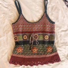 a crocheted tank top with flowers on the front and side, sitting on a bed