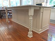 an island in the middle of a kitchen with wooden floors and white cabinetry on both sides