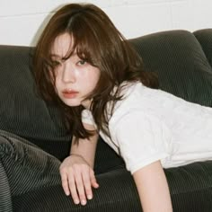 a woman laying on top of a black couch next to a white wall and floor