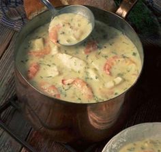 a pot filled with shrimp and cheese soup on top of a wooden table next to bread