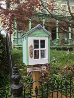 a little green house sitting on top of a wooden post in front of a fence