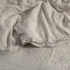 an unmade bed with white linens and buttons on the pillow cover is shown