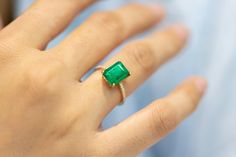 a close up of a person's hand wearing a ring with a green stone