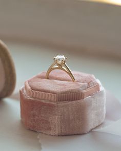 an engagement ring sitting on top of a pink velvet box