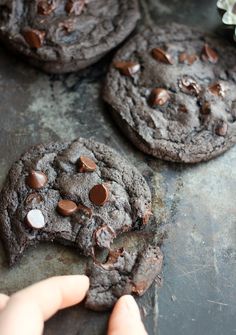 three chocolate cookies on a baking sheet with one broken in half and the other uncooked