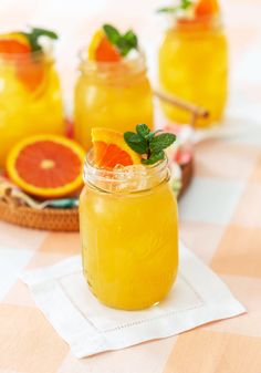 three mason jars filled with orange juice and garnished with mint leaves, sitting on a checkered tablecloth