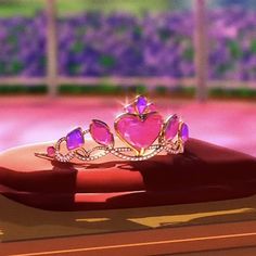 a pink heart shaped tiara sitting on top of a red table with purple flowers in the background