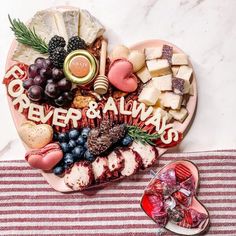 a heart shaped platter filled with cheeses, crackers and fruit sits on a striped tablecloth