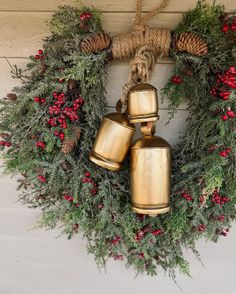 three golden bells hanging from a wreath on the wall with red berries and pine cones