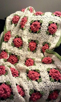 a crocheted blanket with pink and white flowers on it, sitting on a chair