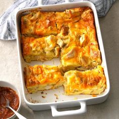 a casserole dish with meat and cheese in it next to a bowl of sauce