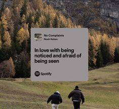 two people walking down a hill with trees in the background and a sign that says, in love with being noticed and afraid of being seen