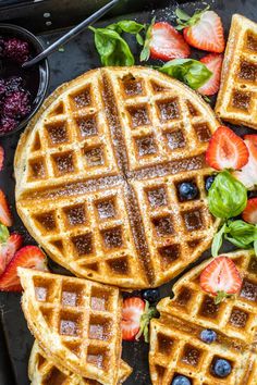 waffles with syrup and strawberries on a black tray next to some fruit