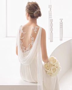 the back of a woman in a white dress with flowers on her shoulder and veil draped over her shoulders