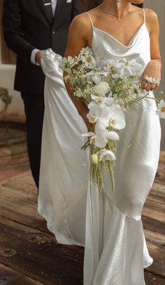 the bride is walking down the aisle with her bouquet in hand and she is wearing a white dress