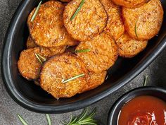 some meat patties in a black bowl with sauces and herbs on the side