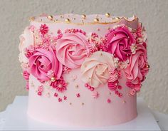 a pink and gold decorated cake with flowers on the top is sitting on a table